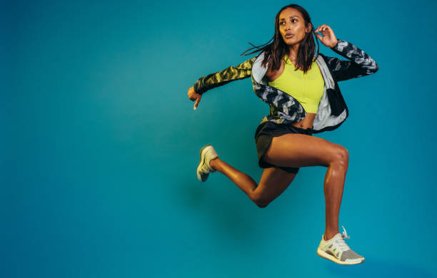 Fit woman training in studio Full length of fit young woman running. Female runner sprinting on blue background with copy space. womens track stock pictures, royalty-free photos & images