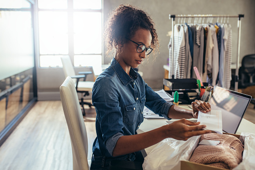 Woman placing the invoice paper inside the product delivery box. Female entrepreneur preparing a package for delivery.