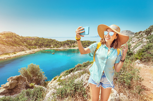 Asian Girl in a hat takes a selfie on the background of stunning views of the azure Bay in the Mediterranean sea. Travel, vacation and mobile connection concept