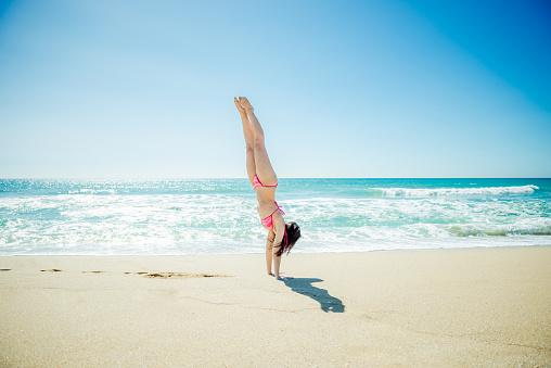 Happy young woman playing handstand on the beach in a hot summer day.