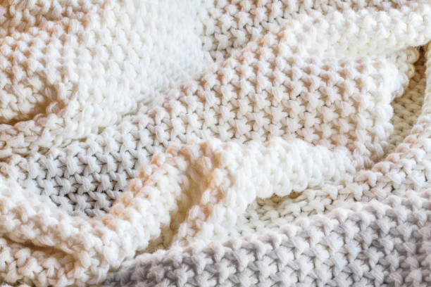 Abstract of a soft knit white and grey throw blanket with selective focus in center with blurred edges.