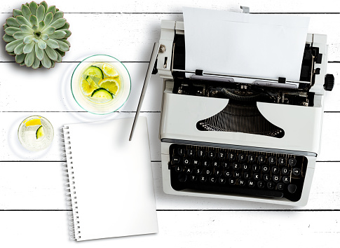 top view of old typewriter, succulent plant, water carafe and notepad on rustic white wooden table