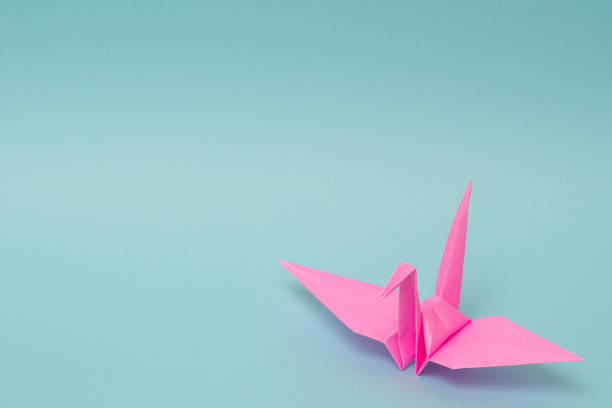 istock pink origami paper crane on sky blue background 1158806493