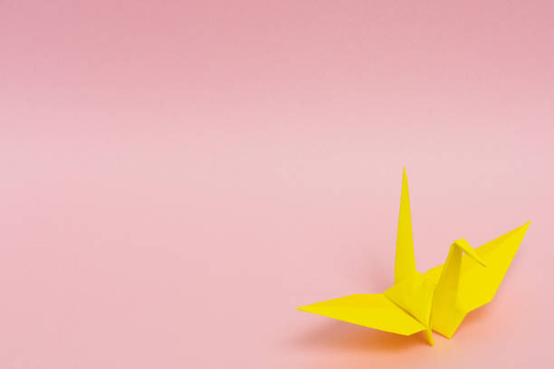 istock yellow origami paper crane on pink background 1158806599