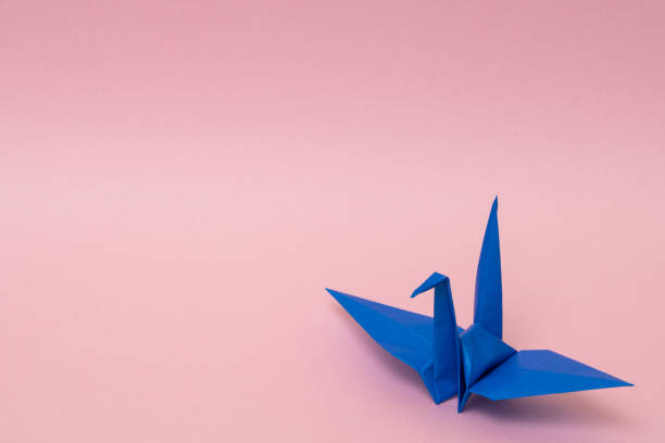 istock blue origami paper crane on pink background 1158806601