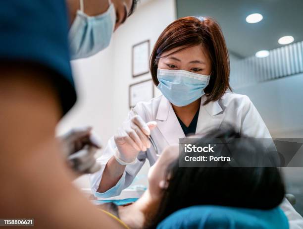 Dentist With Male Assistant Treating Female Patient Stock Photo - Download Image Now