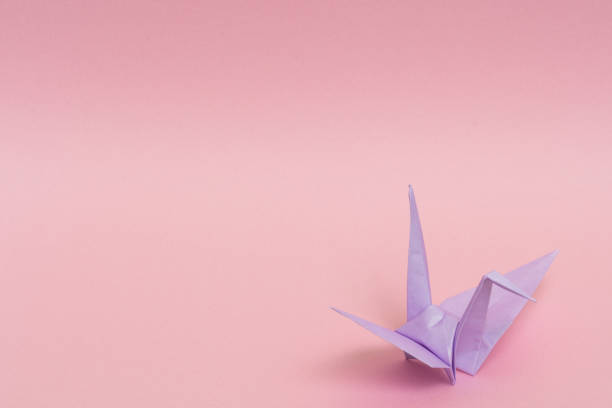 istock light purple origami paper crane on pink background 1158806676