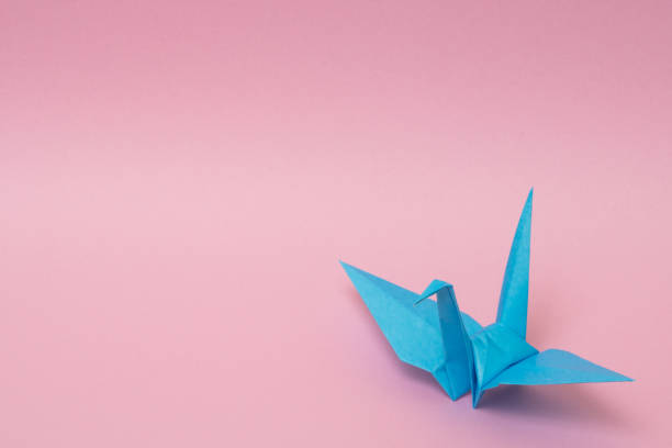 istock light blue origami paper crane on pink background 1158806825