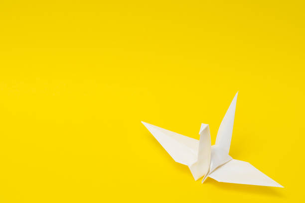istock white origami paper crane on yellow background 1158806972