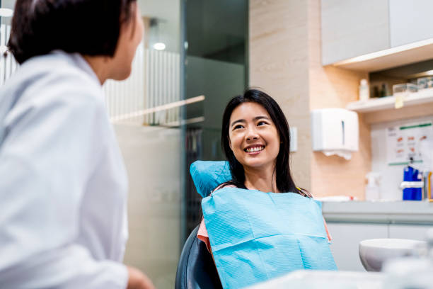 lächelnder patient mit blick auf zahnarzt in klinik - zahnarztstuhl stock-fotos und bilder