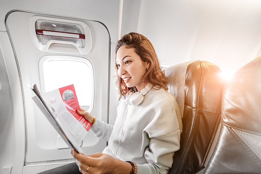 Happy Asian Woman reading magazine in airplane, vacation and leisure concept