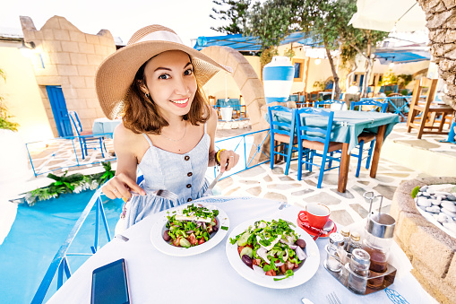 Young elegant girl in the restaurant seasoning salad with olive oil. Concept of Greek cuisine and fresh vegetables