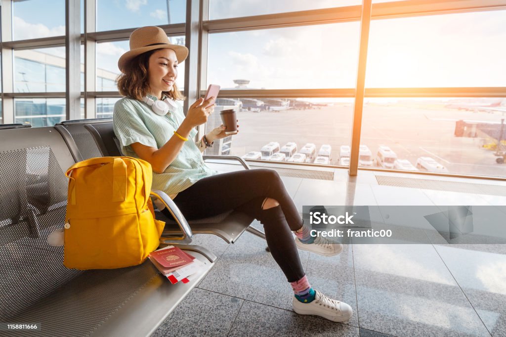 Happy asian woman waiting for her airplane in airport with passport and baggage. Vacation and journey concept Airport Stock Photo