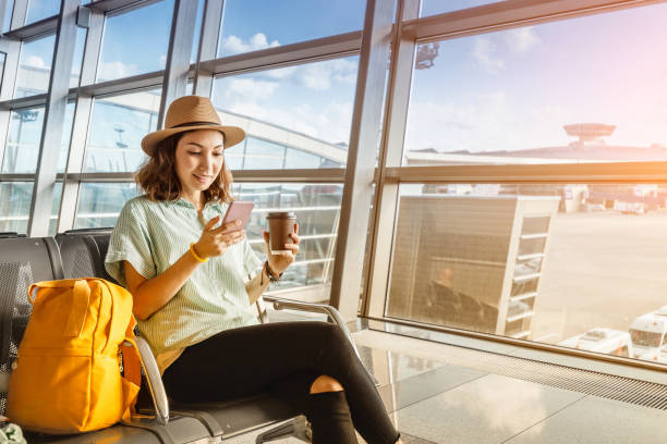 menina asiática que espera a partida no aeroporto em suas férias. usa um smartphone e bebe café - airport airplane travel airport lounge - fotografias e filmes do acervo