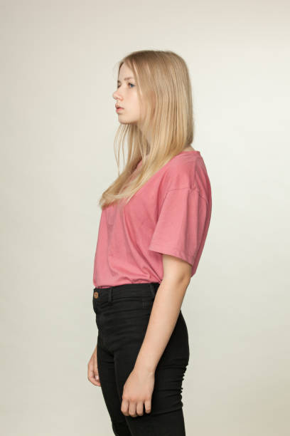Studio portrait of a blonde teen girl in a pink t-shirt and black jeans on a beige background Studio portrait of a blonde teen girl in a pink t-shirt and black jeans on a beige background 15 year old blonde girl stock pictures, royalty-free photos & images