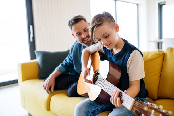 istock Mature father with small son sitting on sofa indoors, playing guitar. 1158815054