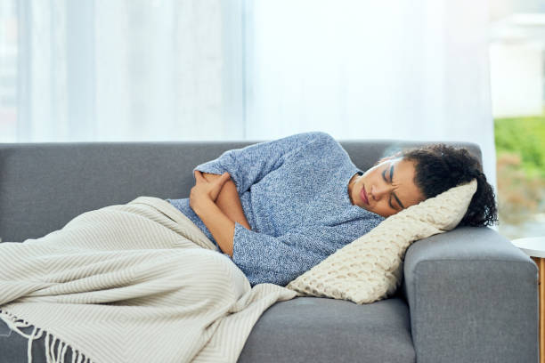 I need painkiller and a hot water bottle Shot of a young woman experiencing stomach pain on the sofa at home pms photos stock pictures, royalty-free photos & images
