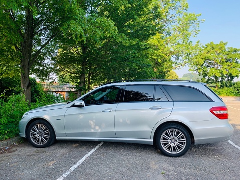 Oberstenfeld, Germany - June, 27 2019: Silver Mercedes-Benz E-Class T in public parking spot under green trees, summer.