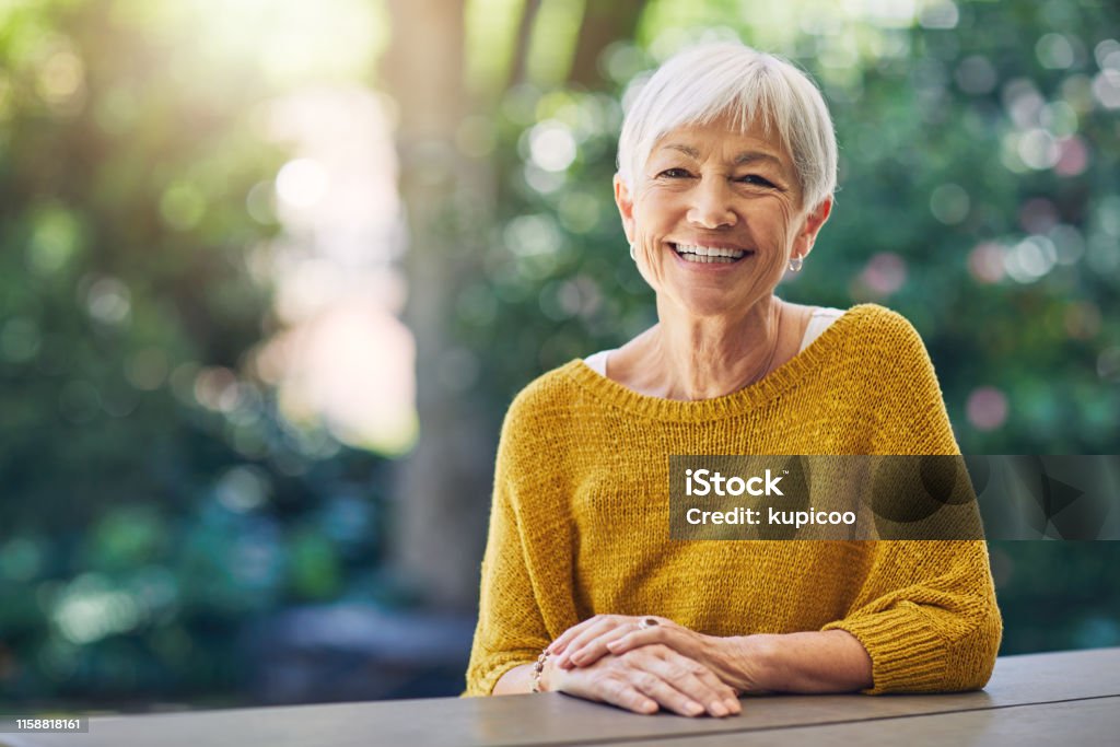 Life's about the moments that made you smile Shot of a happy senior woman sitting at a table in her backyard Senior Adult Stock Photo