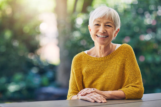 Life's about the moments that made you smile Shot of a happy senior woman sitting at a table in her backyard smiling stock pictures, royalty-free photos & images