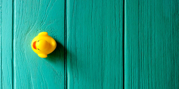 istock Yellow rubber duck on a turquoise colored wooden grained background, conceptually representing water. 1158819608