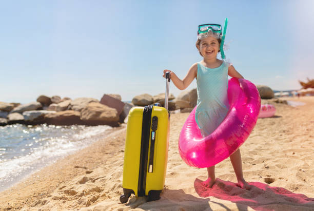 istock Cute child with a inflatable ring and a suitcase on a beach 1158819790