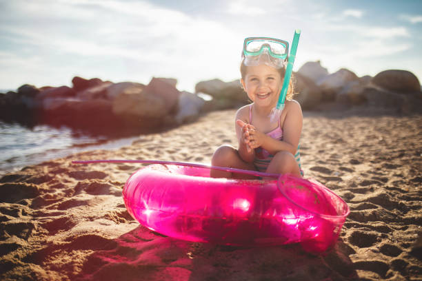 Cute and gorgeous child with a swimming ring and a scuba mask on the beach during summer.