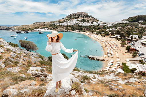 Happy asian woman travels in Greece. Having fun at the stunning view on sea resort and old town of Lindos on the mountain