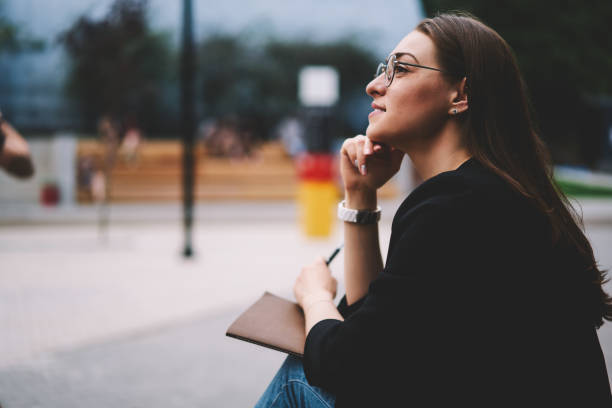 istock Dreaming woman resting outdoors and thinking about end of university while sitting with notepad on urban setting, positive female student 20s feeling pondering after doing homework in textbook 1158824275