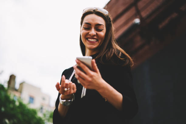istock Attractive successful woman checking funny notification on smartphone from mobile operator while strolling at street.Cheerful teenager having fun during summer walk at urban setting with device 1158824391