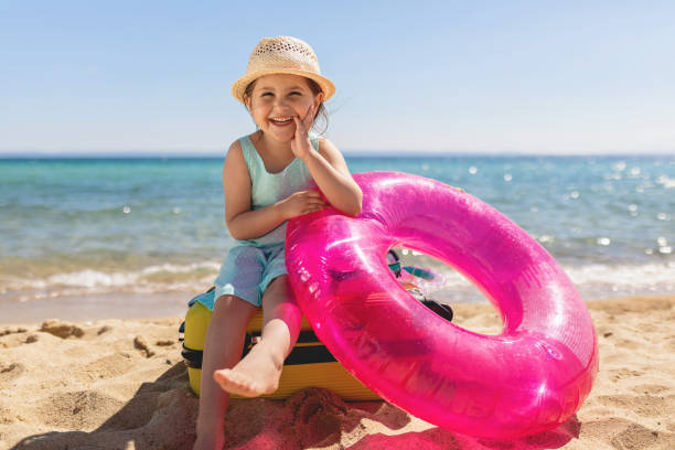 istock Cute tourist child sitting on a suitcase on the beach 1158824585