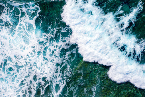Sea waves seen from above, while splashing and flowing on a rocky seabed. Blue and cold hues. Aerial view.