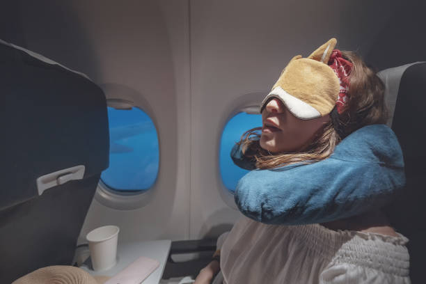 glückliche und müde junge frau bequem schlafen mit maske und kissen im flugzeug. ausgeklügeltes reisekonzept - comfortably stock-fotos und bilder