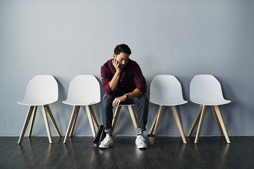 Full length shot of a handsome young businessman sitting and looking down at his watch against a gray studio background