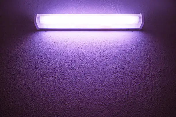 Photo of Germicidal ultraviolet lamp glows on a rough wall.