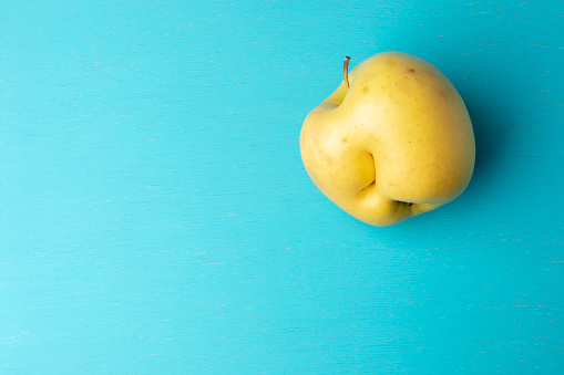 One ugly yellow apple with dent on turquoise painted wooden background. Waste zero concept. Close-up, top view, copy space.