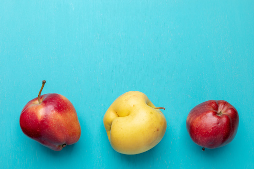 Three ugly red and yellow apples are lying in line in bottom on turquoise painted wooden  background. Waste zero concept. Top view,  flat lay, copy space.