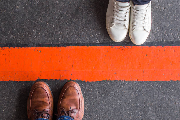 Man and woman divided by a line Man and woman standing opposite each other on either side of the road, divided by a red line. Divorce, breakup, borders, barrier and brexit concept. divider stock pictures, royalty-free photos & images