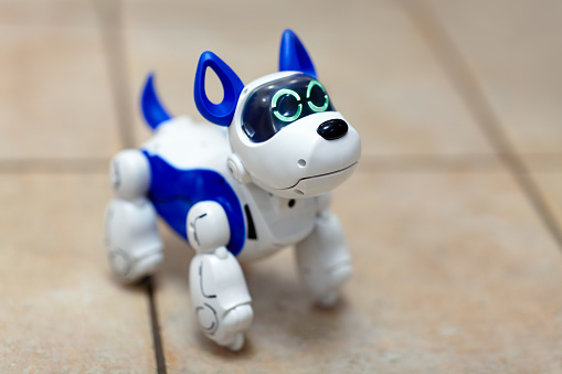 Electronic interactive toy dog puppy on a beige ceramic floor background of selective focus. High technology concept, pet of the future, electronic home. Indoors, copy space, close up.