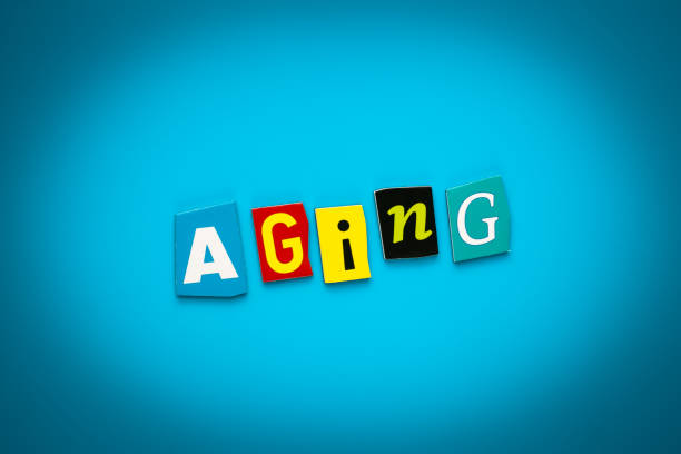 istock Single word - aging - from cut colored letters on blue background. Headline - aging. A word writing text on banner, card. Inscription, message on poster. 1158847312