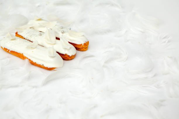 A set of three eclairs with white chocolate decor isolate on a white surface decorated with white feathers