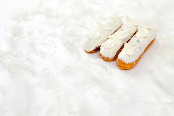 A set of three eclairs with white chocolate decor isolate on a white surface decorated with white feathers