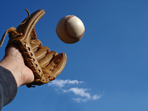Catching a baseball against a blue sky. Right of photo offers negative space.