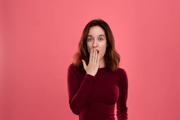 istock Surprised young lady standing isolated over dark pink background with hands raised close to mouth expressing emotion of shock. 1158855038
