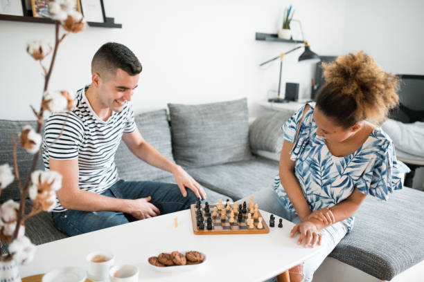 junges heterosexuelles paar sitzt im wohnzimmer und spielt schach - concentration chess playing playful stock-fotos und bilder