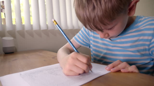 Boy is solving printed labyrinth on paper with pencil at home.