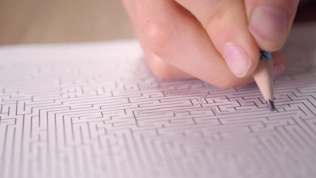 Boy is solving printed labyrinth on paper with pencil at home.