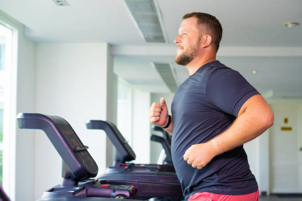 chubby man walking on running track, warming up on gym treadmill. chubby man walking on running track, warming up on gym treadmill overweight man stock pictures, royalty-free photos & images
