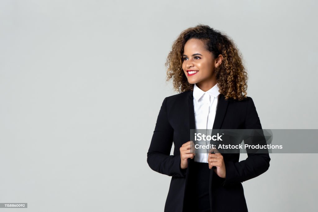 Happy businesswoman in formal clothing Cheerful African American business woman in black suit with curly hair looking away isolated against gray background Women Stock Photo