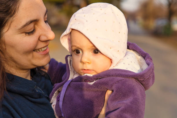 Mother holding a baby daughter in hands outdoors, kissing her.
